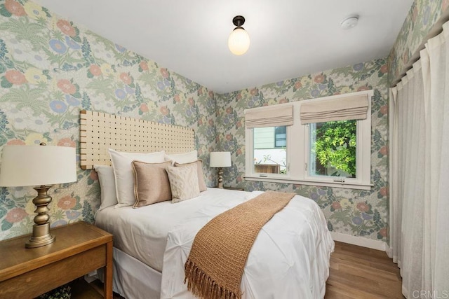 bedroom featuring wallpapered walls, baseboards, and wood finished floors