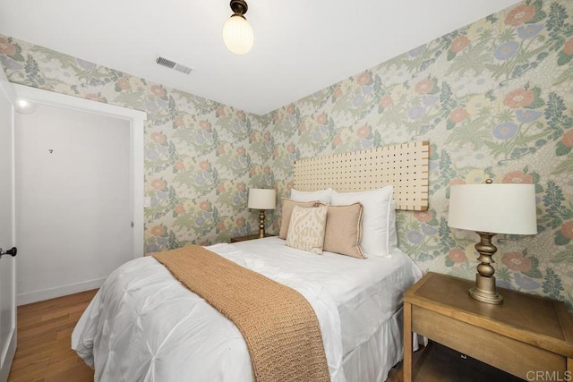 bedroom with baseboards, wallpapered walls, visible vents, and wood finished floors