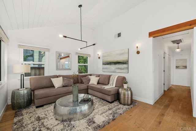 living area with baseboards, visible vents, vaulted ceiling, and wood finished floors