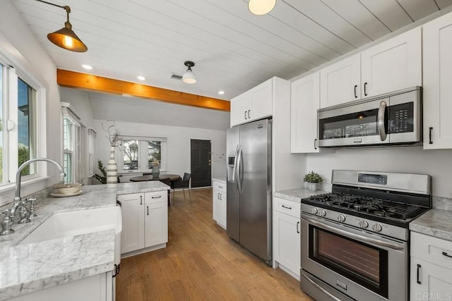 kitchen featuring white cabinetry, light wood-type flooring, stainless steel appliances, a sink, and beamed ceiling