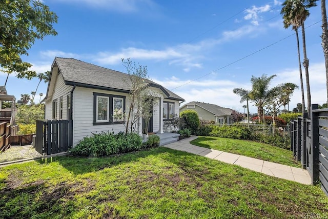 view of front facade with fence, roof with shingles, and a front yard