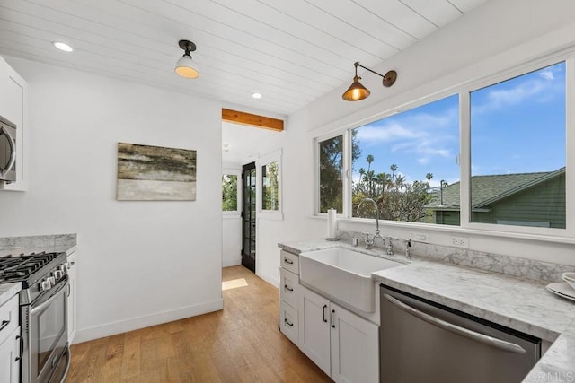 kitchen with white cabinets, a sink, appliances with stainless steel finishes, and light stone countertops