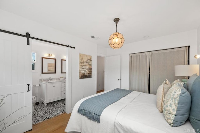 bedroom with connected bathroom, a sink, light wood finished floors, a barn door, and visible vents