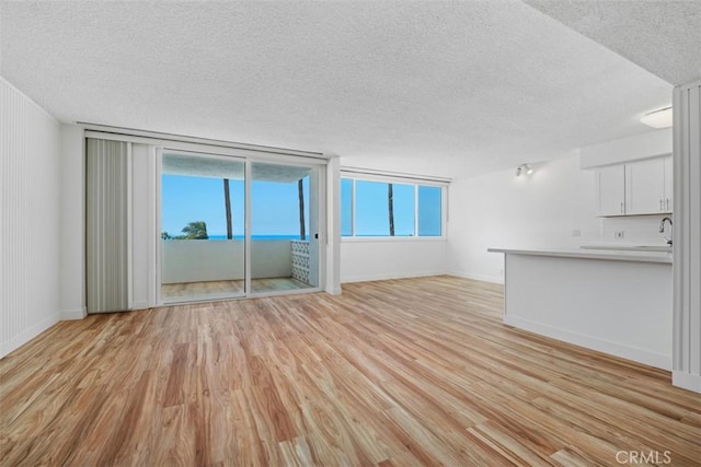 unfurnished living room with a textured ceiling, light wood-style floors, baseboards, and a sink
