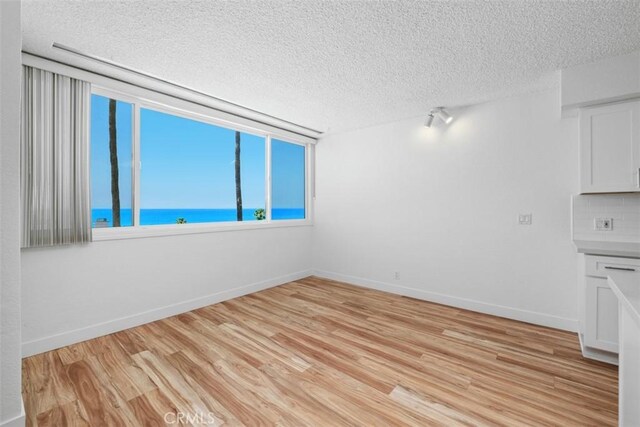 interior space featuring a textured ceiling, light wood-type flooring, baseboards, and a water view