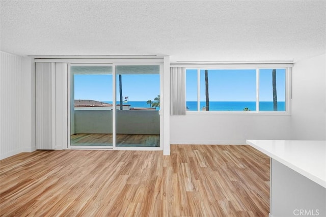 spare room with a textured ceiling, wood finished floors, a water view, and baseboards