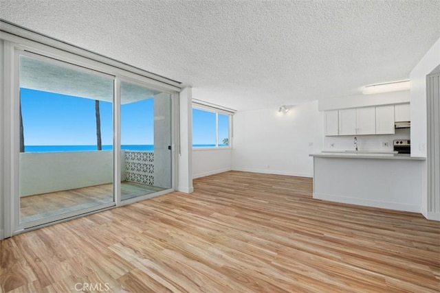 unfurnished living room with a textured ceiling, light wood-style floors, a sink, baseboards, and a water view