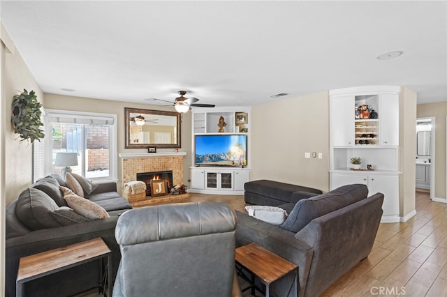 6816 Ridgeside Dr, Riverside, CA 92506 - living area with light wood-type flooring, ceiling fan, a lit fireplace, and built in shelves