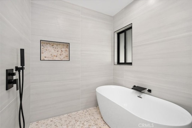 bathroom with tile patterned flooring, tile walls, and a soaking tub