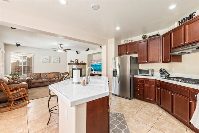 kitchen with light tile patterned floors, a sink, under cabinet range hood, stainless steel appliances, and tile countertops
