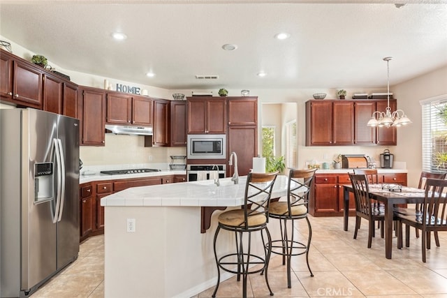 kitchen featuring visible vents, light tile patterned floors, under cabinet range hood, tile counters, and stainless steel appliances