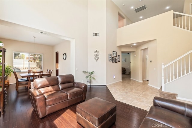 living room featuring visible vents, stairway, a towering ceiling, and light wood finished floors