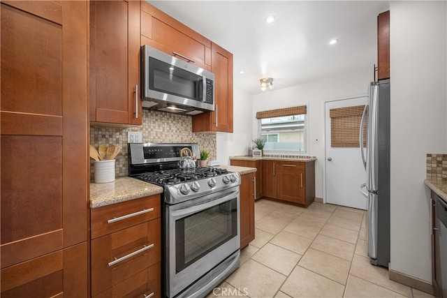 kitchen featuring light stone counters, brown cabinets, light tile patterned floors, backsplash, and appliances with stainless steel finishes