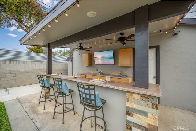 view of patio with ceiling fan, outdoor wet bar, a sink, and fence