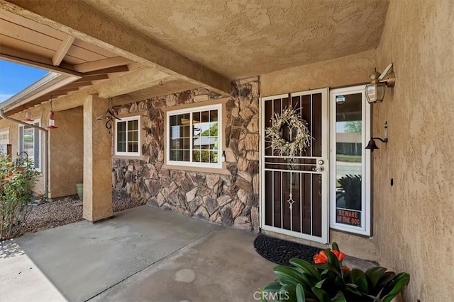property entrance with a patio, stucco siding, and stone siding