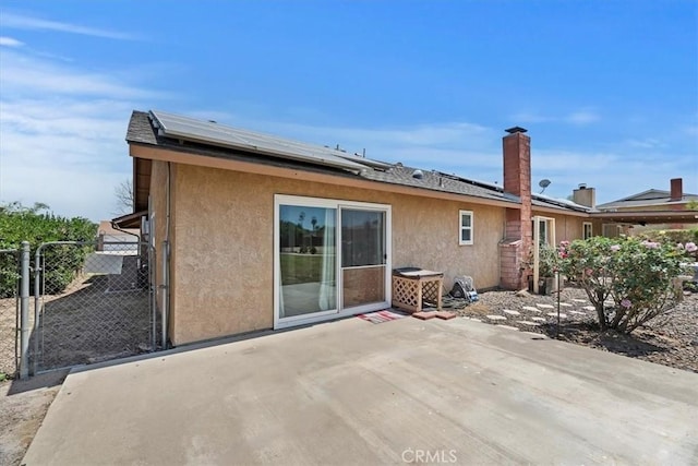 rear view of house featuring a gate, roof mounted solar panels, a patio area, and stucco siding