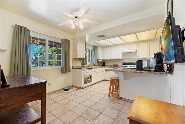 kitchen with white dishwasher, stove, light tile patterned floors, a sink, and a peninsula