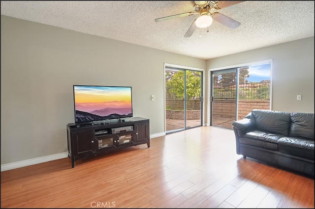 living room with light wood-style floors, a textured ceiling, baseboards, and ceiling fan