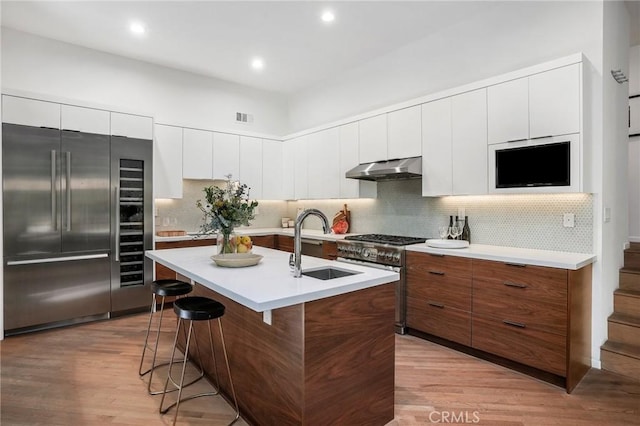 9955 Westwanda Dr, Beverly Hills, CA 90210 - kitchen with premium appliances, a sink, a kitchen breakfast bar, light wood-type flooring, and under cabinet range hood