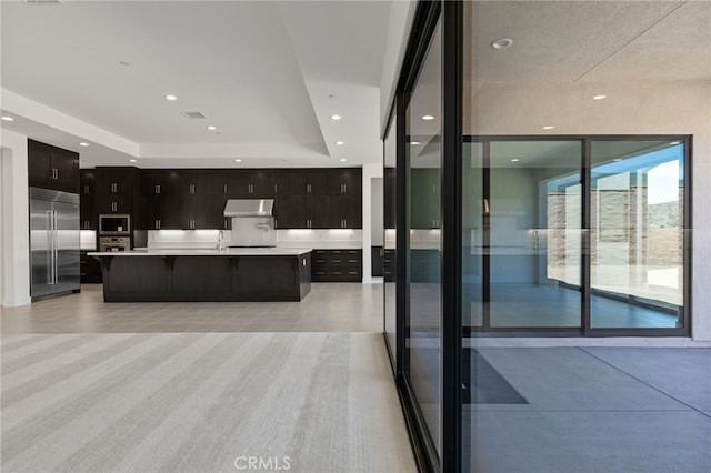 kitchen with a kitchen breakfast bar, built in appliances, light countertops, under cabinet range hood, and a raised ceiling