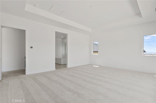 unfurnished bedroom with light colored carpet, baseboards, a walk in closet, and a raised ceiling
