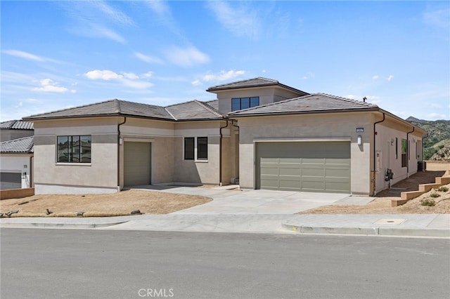 prairie-style home featuring stucco siding, an attached garage, driveway, and a tiled roof