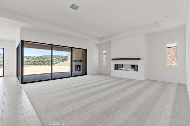 unfurnished living room with plenty of natural light, a glass covered fireplace, light carpet, a tray ceiling, and visible vents