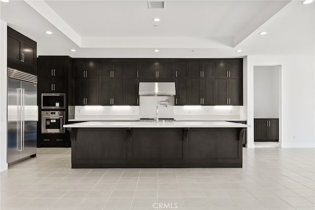 kitchen with wall chimney exhaust hood, built in appliances, light countertops, and a raised ceiling