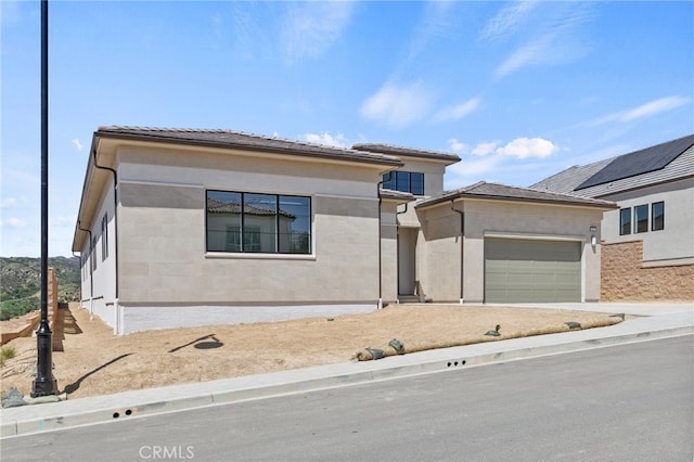 prairie-style home with a garage, concrete driveway, a tiled roof, and stucco siding
