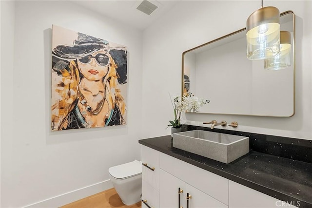 bathroom with toilet, vanity, baseboards, and wood finished floors