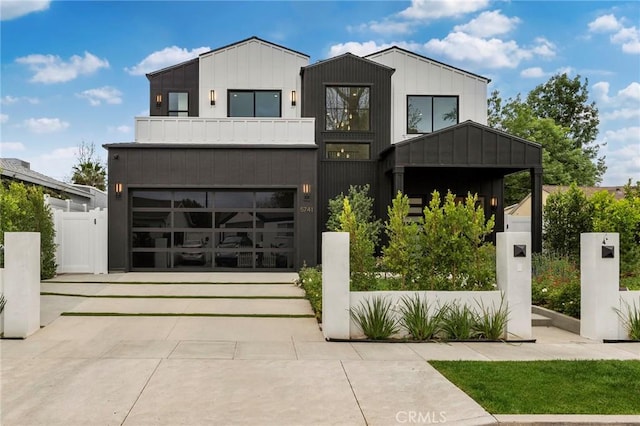 modern home featuring a balcony, driveway, an attached garage, fence, and board and batten siding