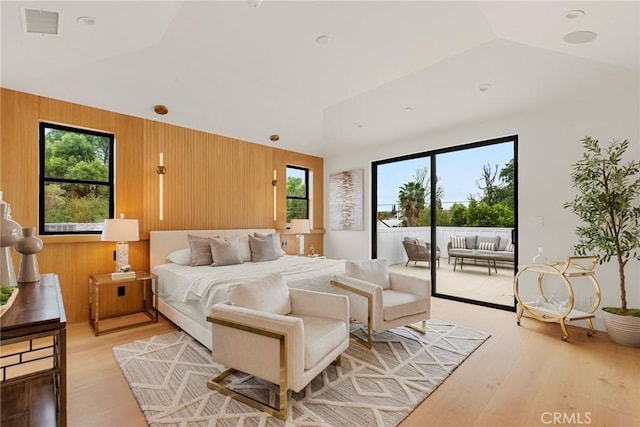 bedroom with access to exterior, multiple windows, lofted ceiling, light wood-style floors, and wooden walls