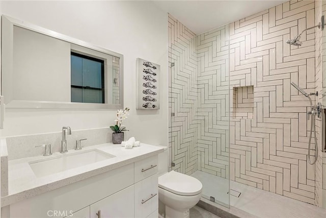bathroom with toilet, tiled shower, and vanity