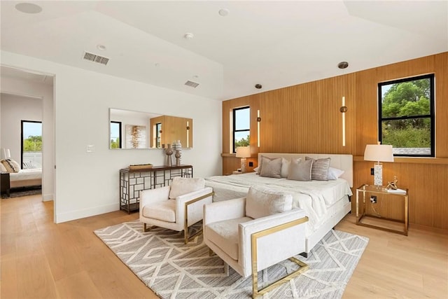 bedroom with multiple windows, wood walls, light wood-style floors, and baseboards