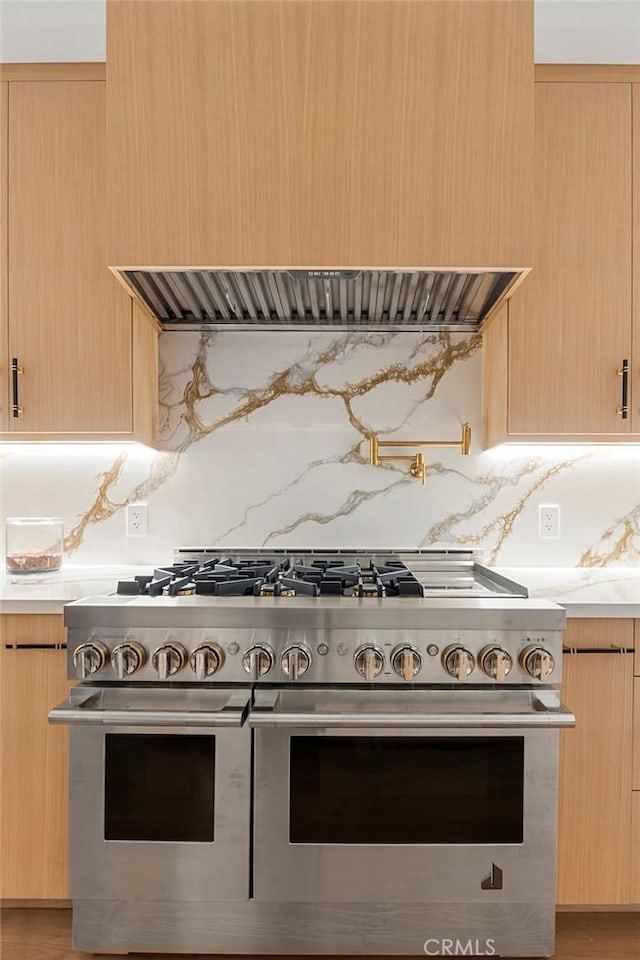 kitchen with range with two ovens, light brown cabinets, tasteful backsplash, range hood, and light wood-style floors