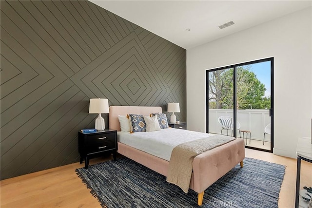 bedroom featuring access to outside, an accent wall, and light wood-type flooring