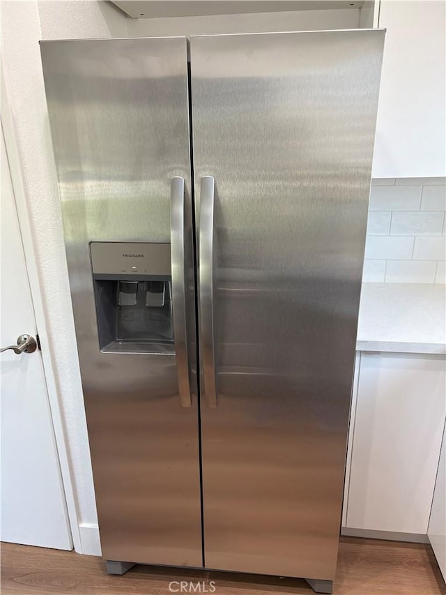 details with light countertops, stainless steel refrigerator with ice dispenser, white cabinets, and wood finished floors