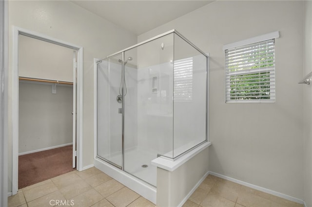 bathroom featuring a spacious closet, tile patterned flooring, baseboards, and a stall shower