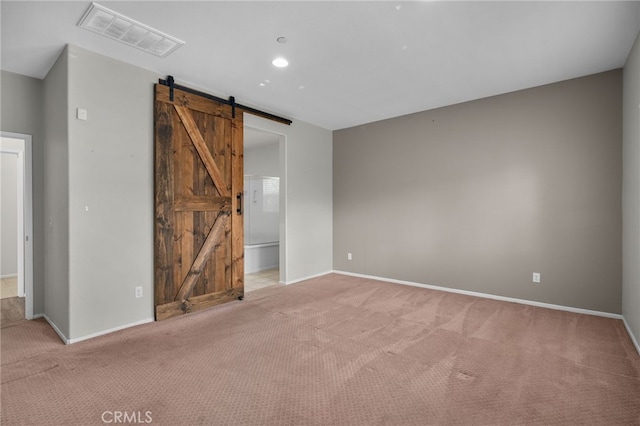 unfurnished bedroom featuring baseboards, carpet, visible vents, and a barn door
