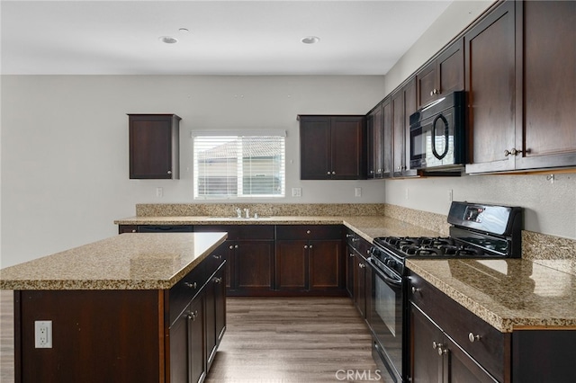 kitchen featuring dark brown cabinetry, black appliances, a kitchen island, wood finished floors, and light countertops