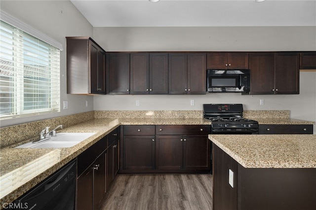kitchen with dark brown cabinets, black appliances, light stone countertops, a sink, and wood finished floors