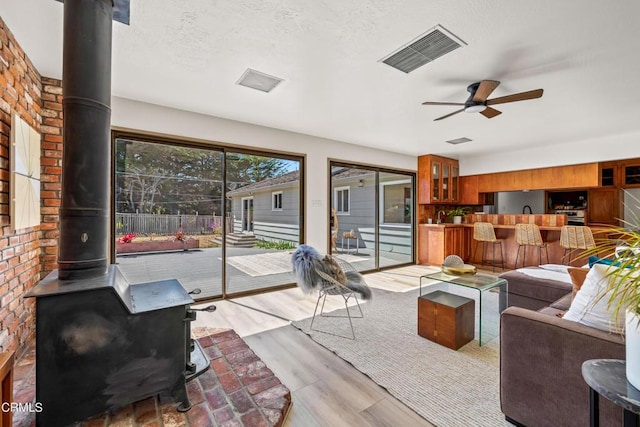 living room with light wood-type flooring, a wood stove, a textured ceiling, visible vents, and a ceiling fan