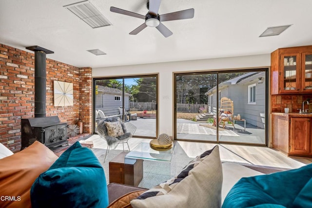 living room featuring a wood stove, brick wall, visible vents, a ceiling fan, and wood finished floors