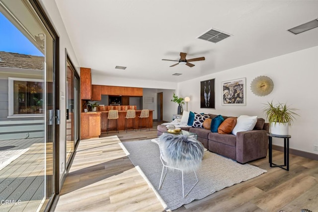 living room featuring baseboards, visible vents, light wood-type flooring, and a ceiling fan