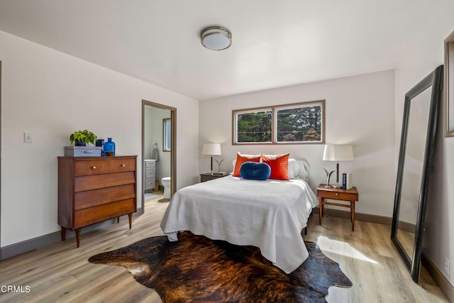 bedroom with baseboards, light wood-style floors, and ensuite bathroom