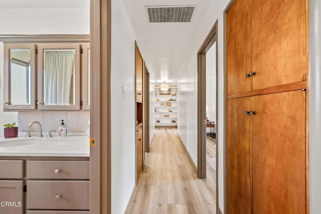 hallway with light wood-type flooring, a sink, and visible vents