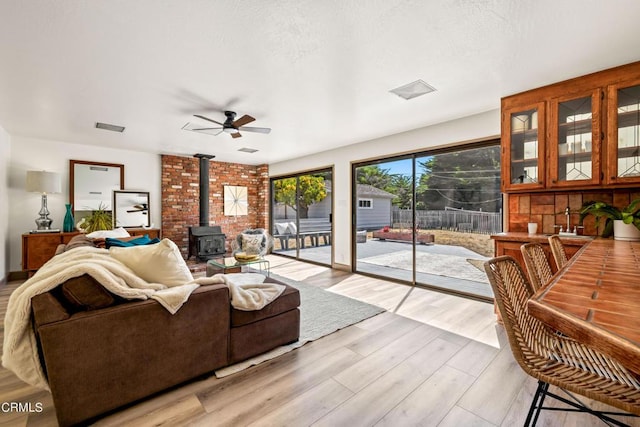 living room with a wood stove, a textured ceiling, light wood-style floors, visible vents, and ceiling fan