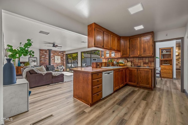 kitchen with light wood-type flooring, a wood stove, a sink, visible vents, and dishwasher