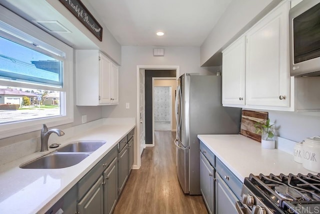kitchen with wood finished floors, a sink, gray cabinets, stainless steel appliances, and white cabinets