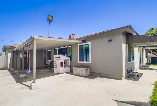 back of property with a chimney, a patio, and stucco siding